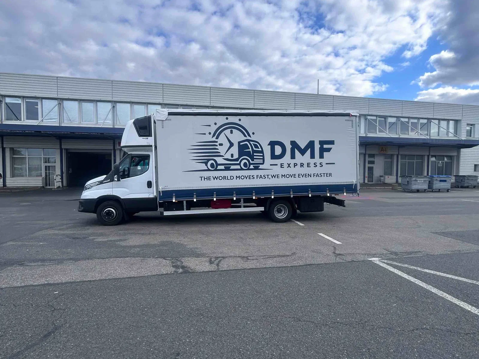 DMF Express 7.2 t curtain-side truck in front of a warehouse with loading docks