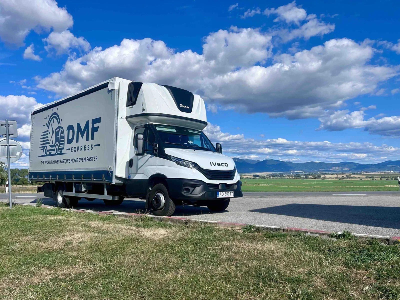 DMF Express curtain-side truck on a country road with fields and mountains behind it