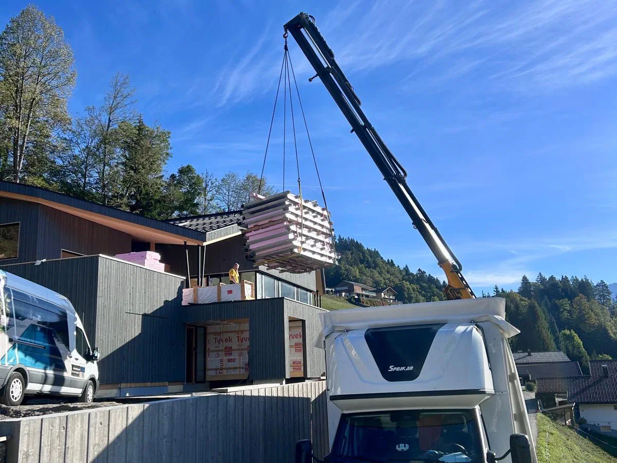 A crane lifting cargo through the open roof of a DMF Express curtain-side truck on an Alpine building site