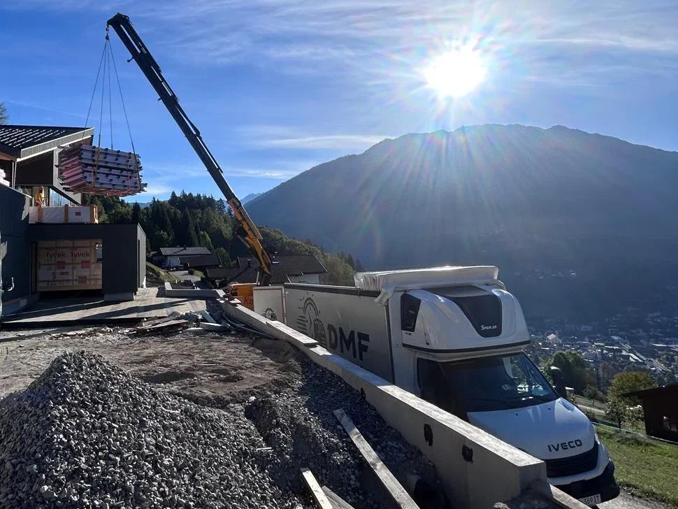 DMF Express curtain-side truck being unloaded by crane at a building site in the Alps